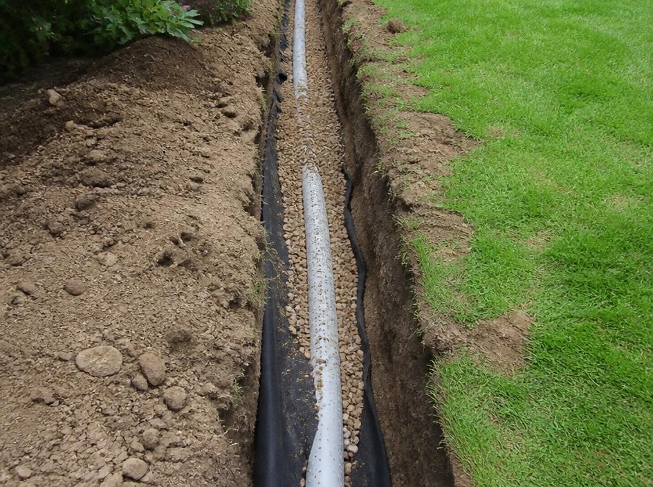 French drain with perforated pipe and gravel in a garden lawn